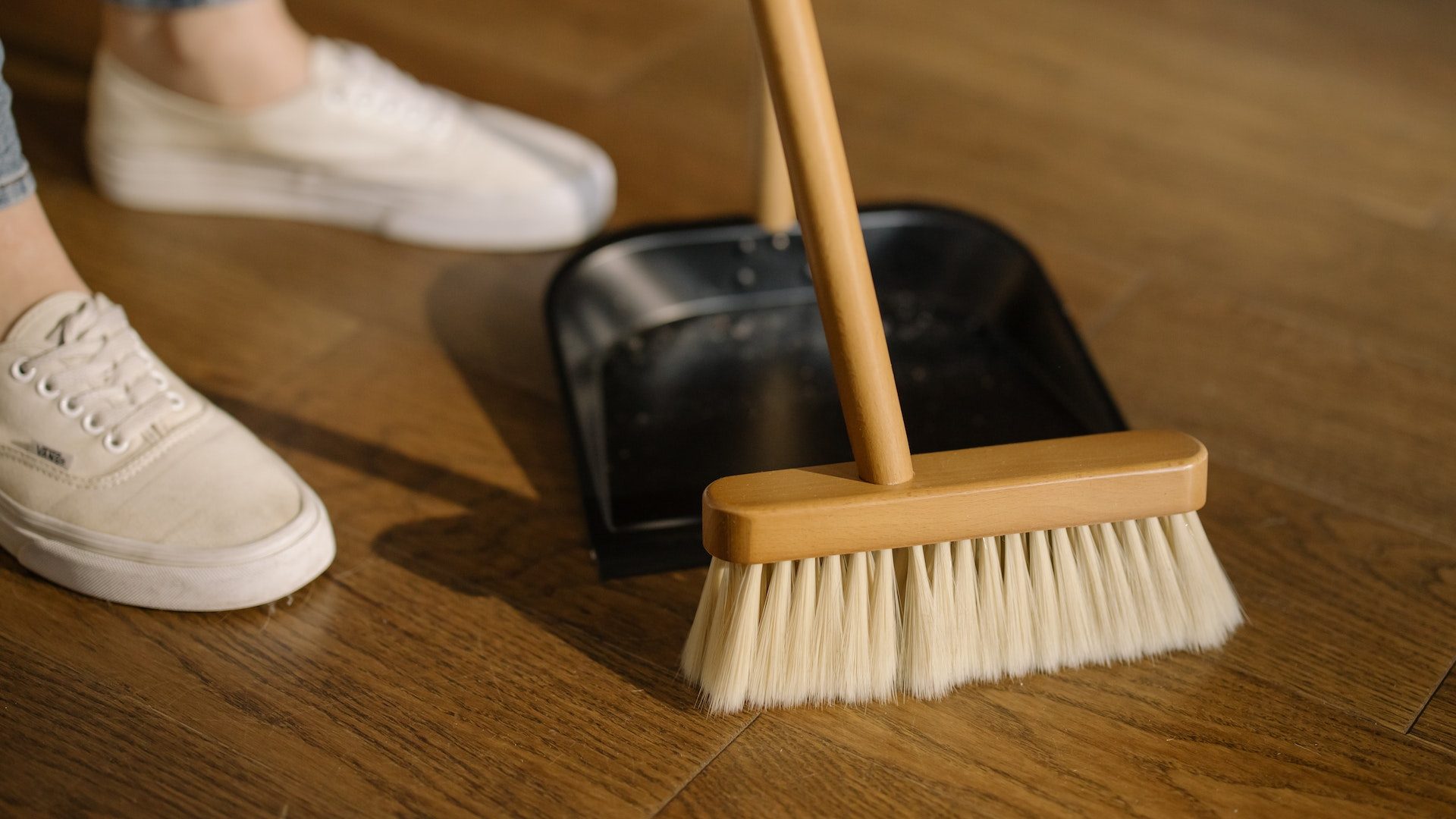 Person Wearing White Pants and White Socks Standing Beside Brown Broom