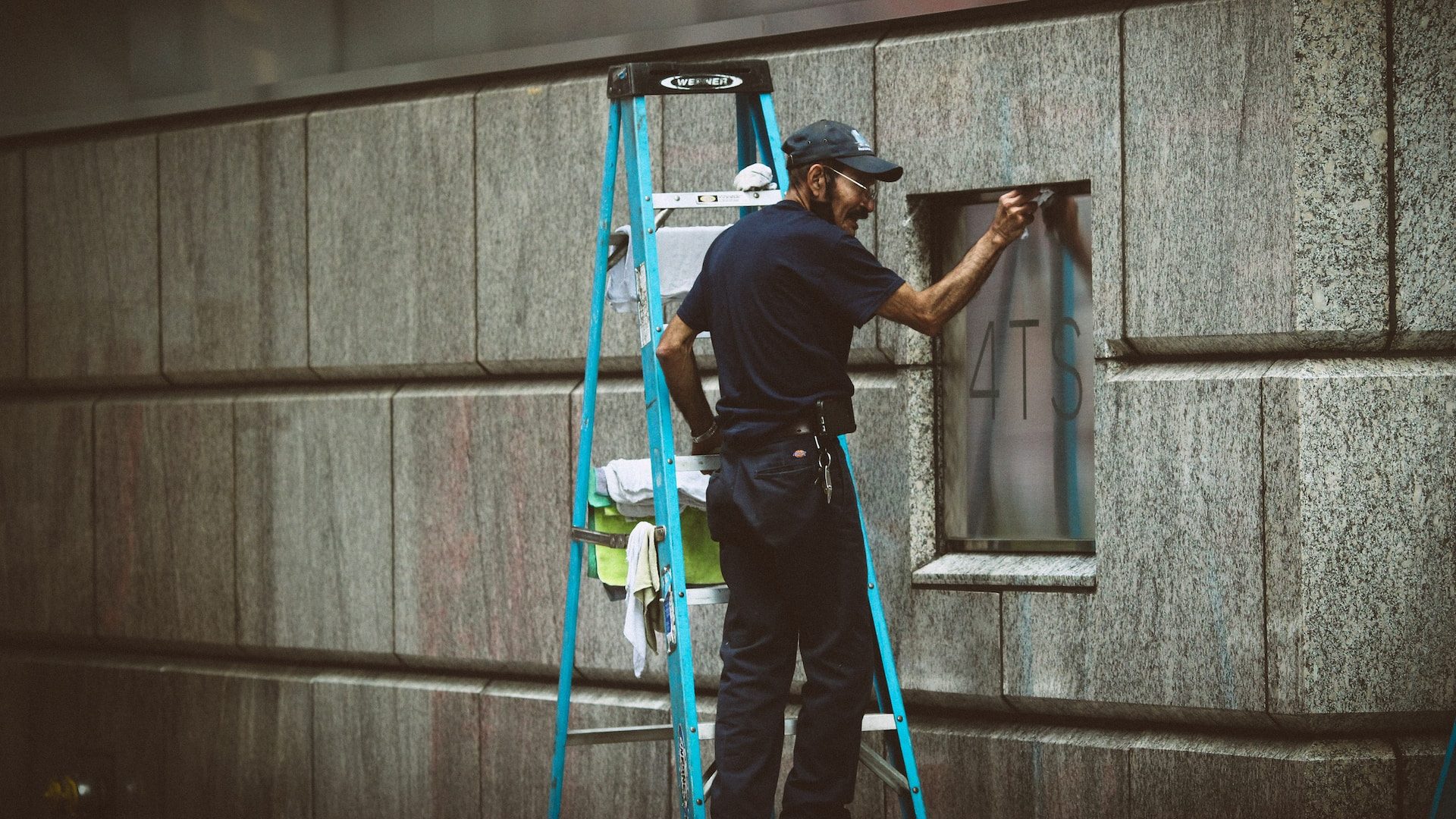 man in blue t-shirt and blue pants standing on ladder